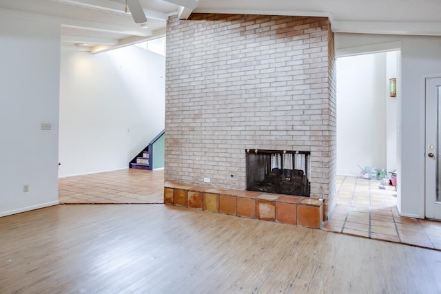 unfurnished living room with lofted ceiling with beams, a brick fireplace, and light wood-type flooring