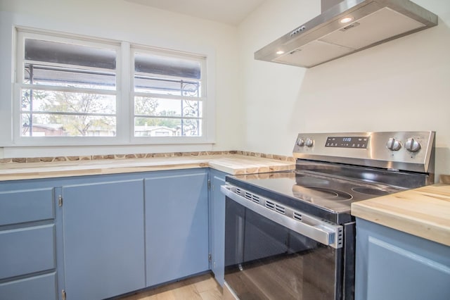 kitchen featuring wood counters, electric range, blue cabinetry, light wood-type flooring, and wall chimney exhaust hood