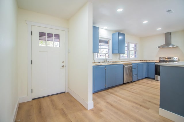 kitchen featuring appliances with stainless steel finishes, sink, blue cabinetry, light wood-type flooring, and wall chimney exhaust hood