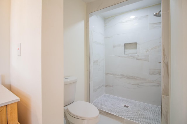 bathroom featuring vanity, a tile shower, and toilet