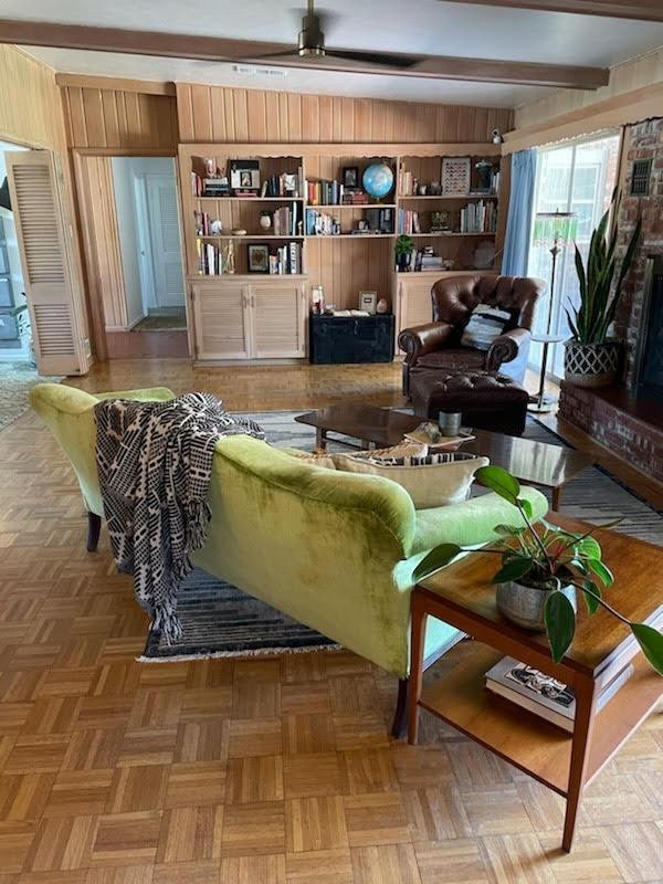 living room with wood walls, built in features, beamed ceiling, ceiling fan, and light parquet flooring