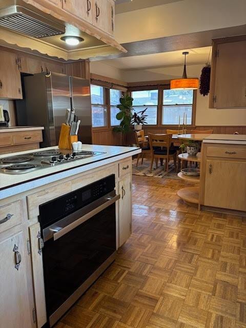 kitchen featuring appliances with stainless steel finishes, parquet flooring, pendant lighting, light brown cabinetry, and exhaust hood