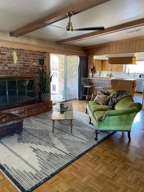 living room featuring a healthy amount of sunlight, a brick fireplace, parquet flooring, and beamed ceiling