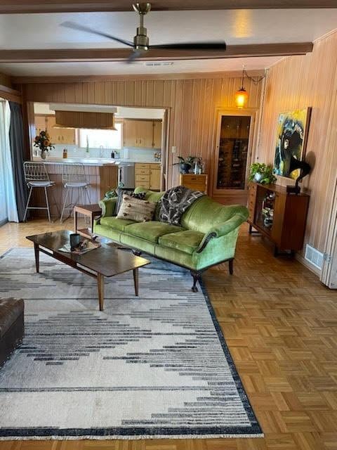 living room featuring ceiling fan, parquet flooring, beam ceiling, and wood walls