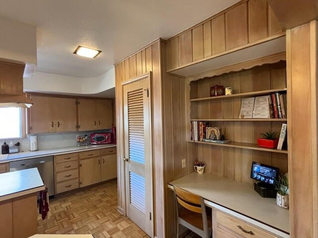 kitchen with backsplash, built in desk, stainless steel dishwasher, and light parquet floors