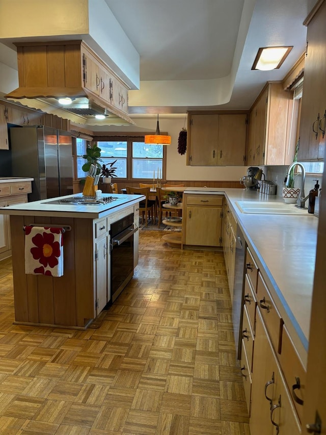 kitchen with sink, hanging light fixtures, appliances with stainless steel finishes, a kitchen island, and light parquet floors