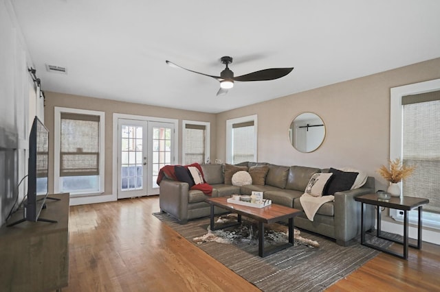 living room featuring wood-type flooring, a barn door, ceiling fan, and french doors