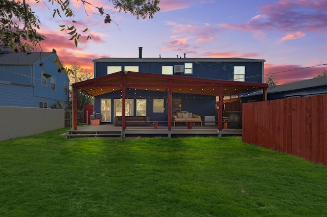 back house at dusk featuring a deck and a lawn