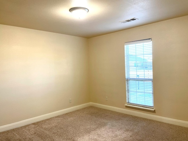 carpeted empty room featuring plenty of natural light, visible vents, and baseboards