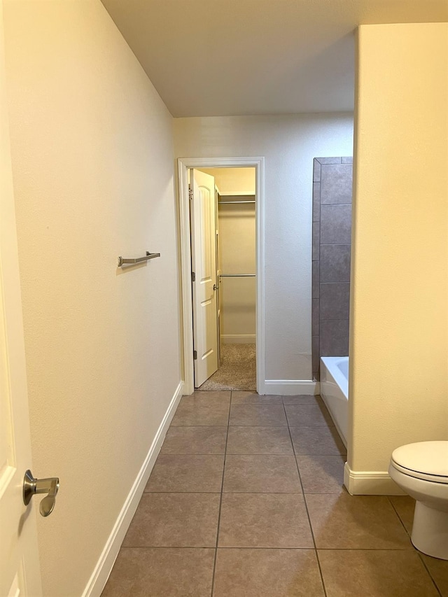 bathroom with toilet, baseboards, tile patterned floors, a walk in closet, and a bathtub