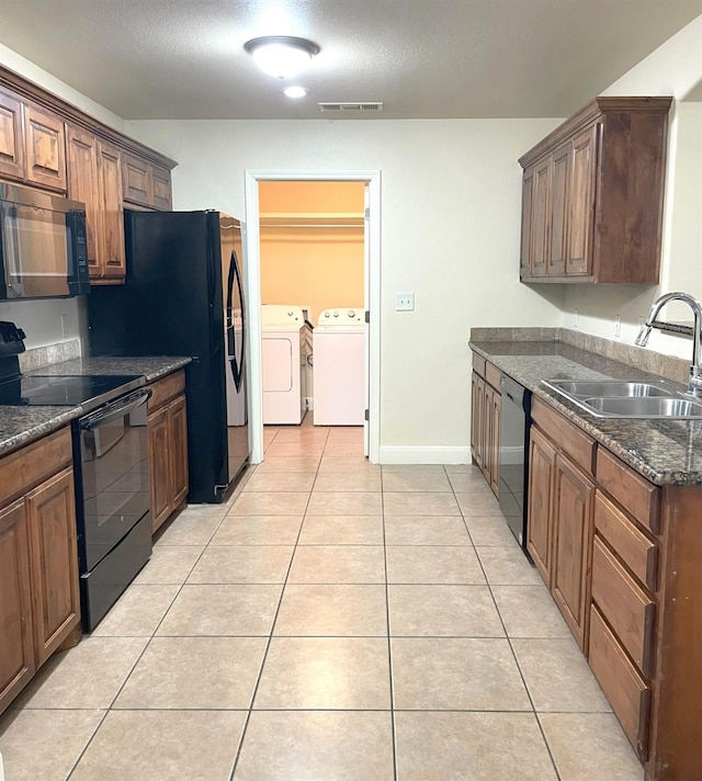 kitchen featuring a sink, black appliances, light tile patterned floors, and washer and dryer