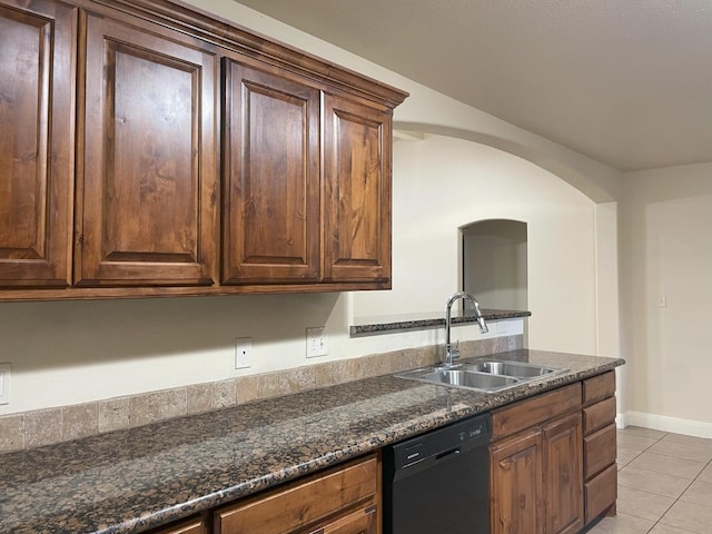 kitchen with light tile patterned floors, baseboards, dishwasher, dark stone countertops, and a sink