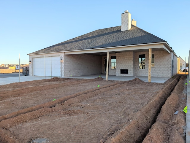 rear view of house featuring an attached garage, brick siding, concrete driveway, a chimney, and a patio area