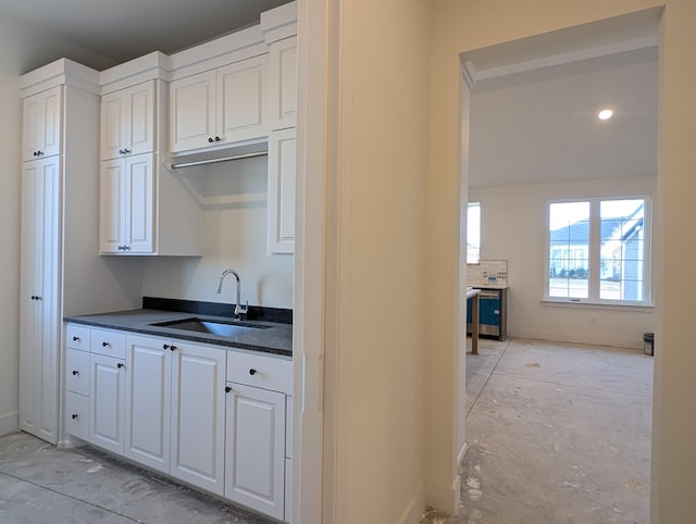 kitchen with dark countertops, white cabinetry, a sink, dishwasher, and baseboards