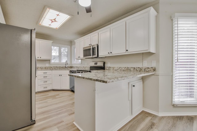 kitchen with light stone counters, light hardwood / wood-style flooring, stainless steel appliances, and white cabinets