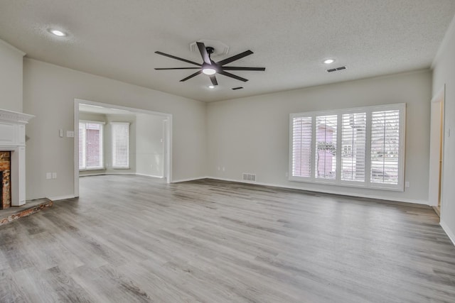 unfurnished living room with ceiling fan, a brick fireplace, a textured ceiling, and light wood-type flooring