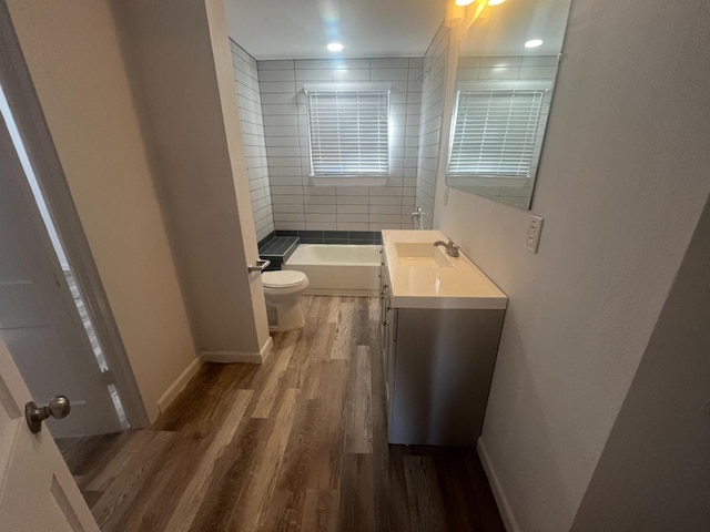 full bathroom with vanity, tiled shower / bath, hardwood / wood-style floors, and toilet