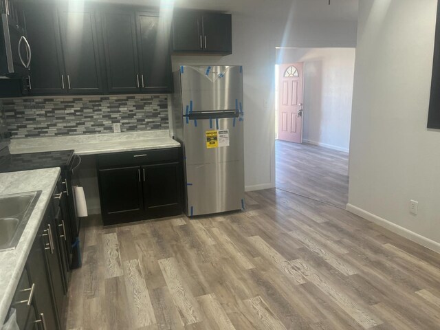 kitchen with tasteful backsplash, light wood-type flooring, light stone countertops, and appliances with stainless steel finishes