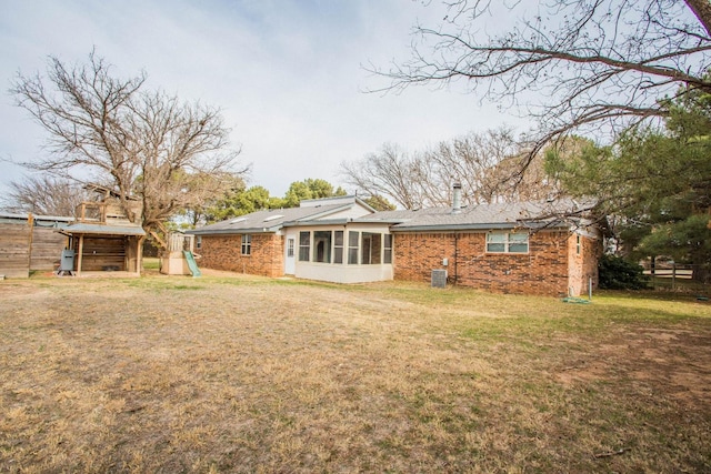 rear view of house featuring central AC unit, a yard, a sunroom, and a playground