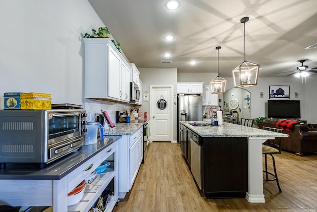 2541 137th St, Lubbock, TX 79423 - kitchen with appliances with stainless steel finishes, a kitchen island with sink, white cabinets, decorative backsplash, and decorative light fixtures