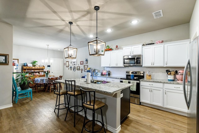 2541 137th St, Lubbock, TX 79423 - kitchen featuring white cabinetry, a kitchen island with sink, stainless steel appliances, light stone countertops, and decorative light fixtures