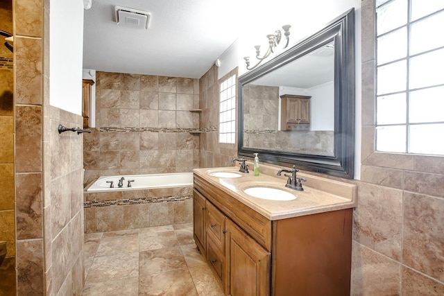 bathroom with a relaxing tiled tub, vanity, and tile walls