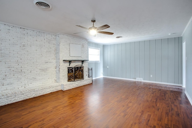 unfurnished living room with brick wall, ceiling fan, crown molding, a brick fireplace, and dark wood-type flooring