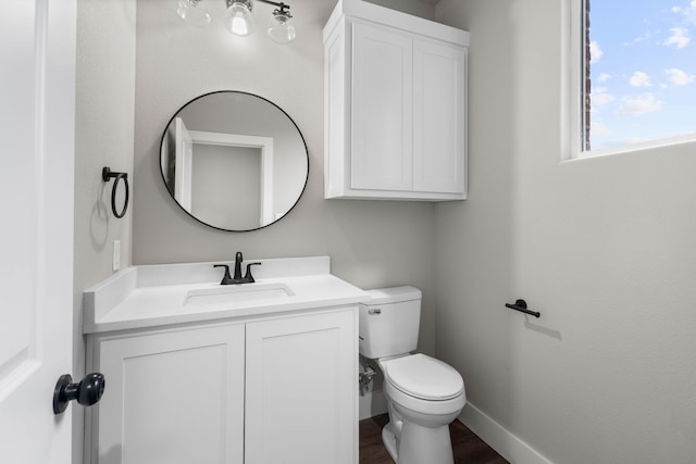 half bath with toilet, wood finished floors, vanity, and baseboards