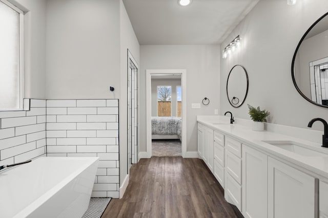 full bath with double vanity, a sink, a freestanding bath, and wood finished floors