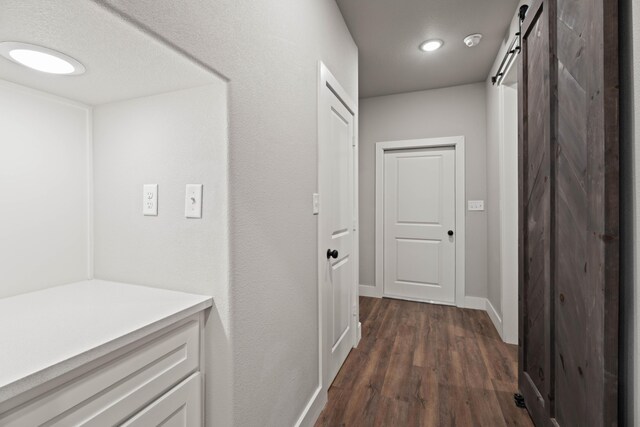 corridor with dark wood-style flooring, baseboards, and a barn door