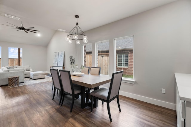 dining area with vaulted ceiling, dark wood-type flooring, ceiling fan with notable chandelier, and baseboards