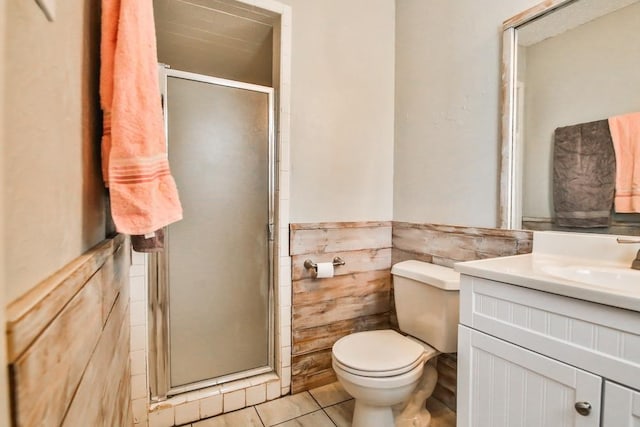 bathroom with tile patterned floors, toilet, tile walls, vanity, and a shower with door