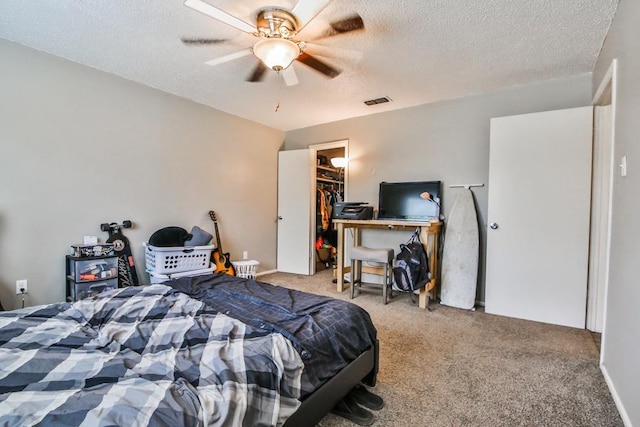 carpeted bedroom with ceiling fan, a closet, a textured ceiling, and a walk in closet