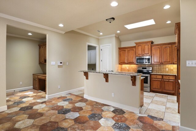 kitchen with a skylight, a kitchen breakfast bar, stainless steel appliances, an island with sink, and decorative backsplash