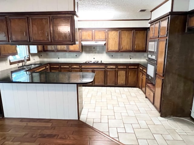 kitchen with sink, decorative backsplash, wall oven, dark brown cabinets, and a textured ceiling