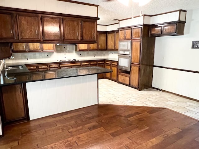 kitchen featuring dark brown cabinets, white microwave, a textured ceiling, stainless steel oven, and light wood-type flooring