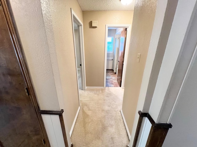 hall with light colored carpet and a textured ceiling