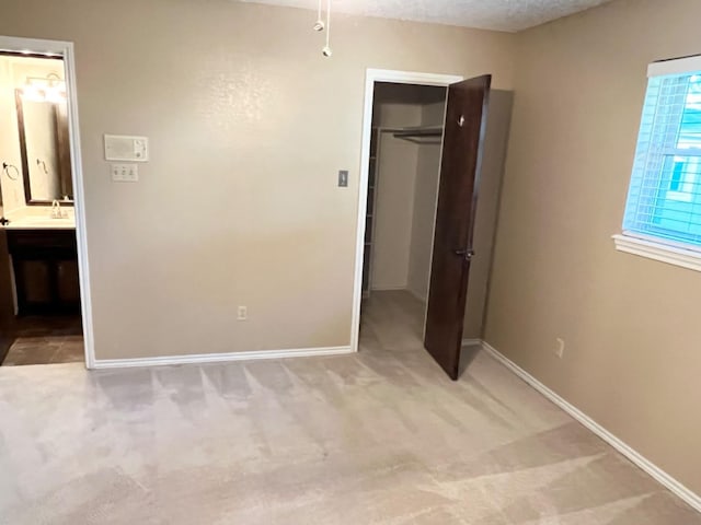 unfurnished bedroom with sink, ensuite bathroom, carpet flooring, a spacious closet, and a closet