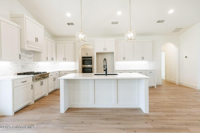 7450 55th St, Lubbock, TX 79407 - kitchen featuring a sink, appliances with stainless steel finishes, a kitchen island with sink, backsplash, and arched walkways