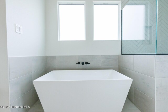 7450 55th St, Lubbock, TX 79407 - bathroom featuring tile walls, a freestanding bath, and tile patterned flooring