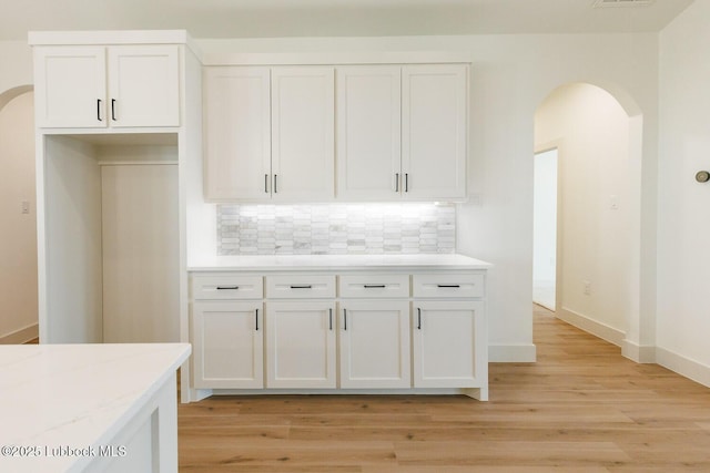 7450 55th St, Lubbock, TX 79407 - kitchen with arched walkways, decorative backsplash, white cabinets, and light wood-style flooring
