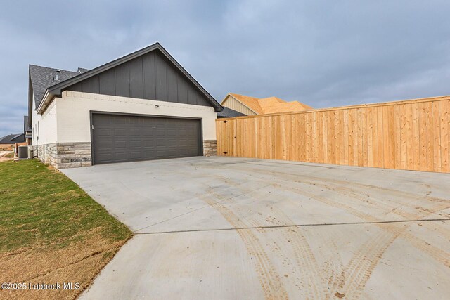 7450 55th St, Lubbock, TX 79407 - view of home's exterior with stone siding, cooling unit, concrete driveway, board and batten siding, and an attached garage
