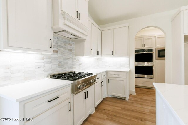 7450 55th St, Lubbock, TX 79407 - kitchen with stainless steel appliances, white cabinetry, light wood-style floors, decorative backsplash, and arched walkways