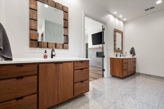 bathroom with two vanities, speckled floor, visible vents, a sink, and baseboards