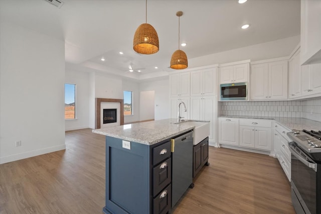 kitchen featuring sink, decorative light fixtures, an island with sink, stainless steel appliances, and white cabinets