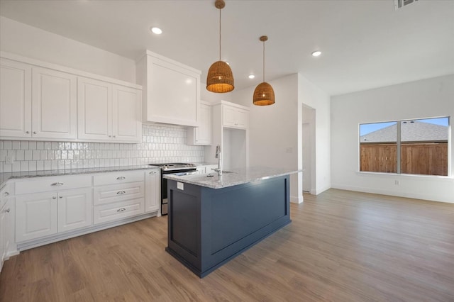 kitchen with an island with sink, pendant lighting, stainless steel range with gas stovetop, and white cabinets