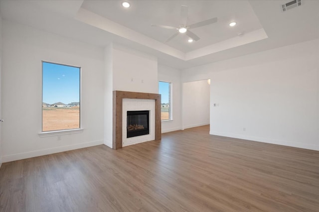 unfurnished living room featuring light hardwood / wood-style flooring, ceiling fan, and a tray ceiling