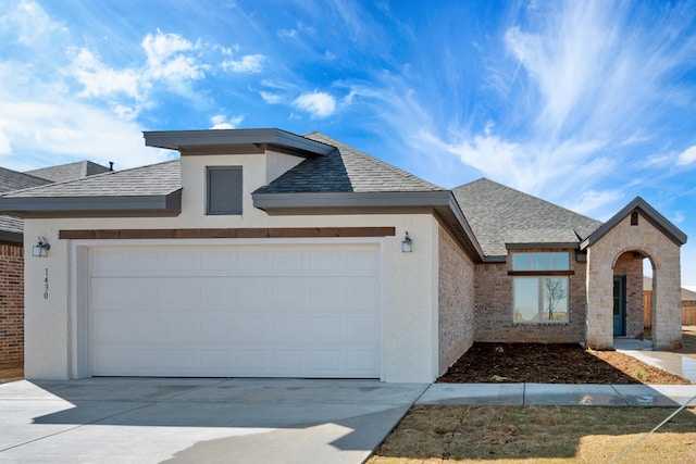 view of front of property featuring roof with shingles, a garage, driveway, and stucco siding