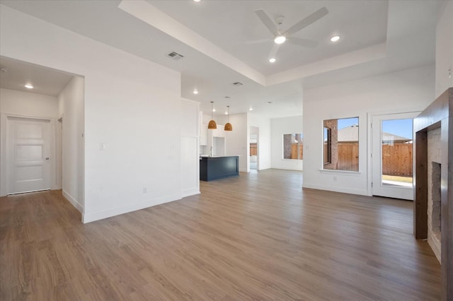 unfurnished living room with hardwood / wood-style flooring, a raised ceiling, and ceiling fan