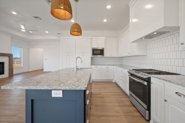 kitchen with stainless steel appliances, custom range hood, and a center island with sink